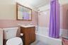 Bathroom with pink tiled walls, a white bathtub with shower fixture, a wood-finish vanity with an integrated sink, and a framed mirrored medicine cabi