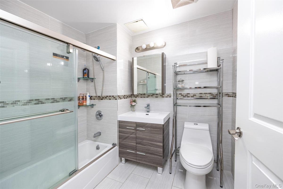 Full bath with tile walls, combined bath / shower with glass door, vanity, and light tile patterned floors