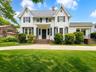 Stunning front façade highlighted by classic architectural styling, symmetrical design, and mature landscaping. The expansive lawn, inviting covered e