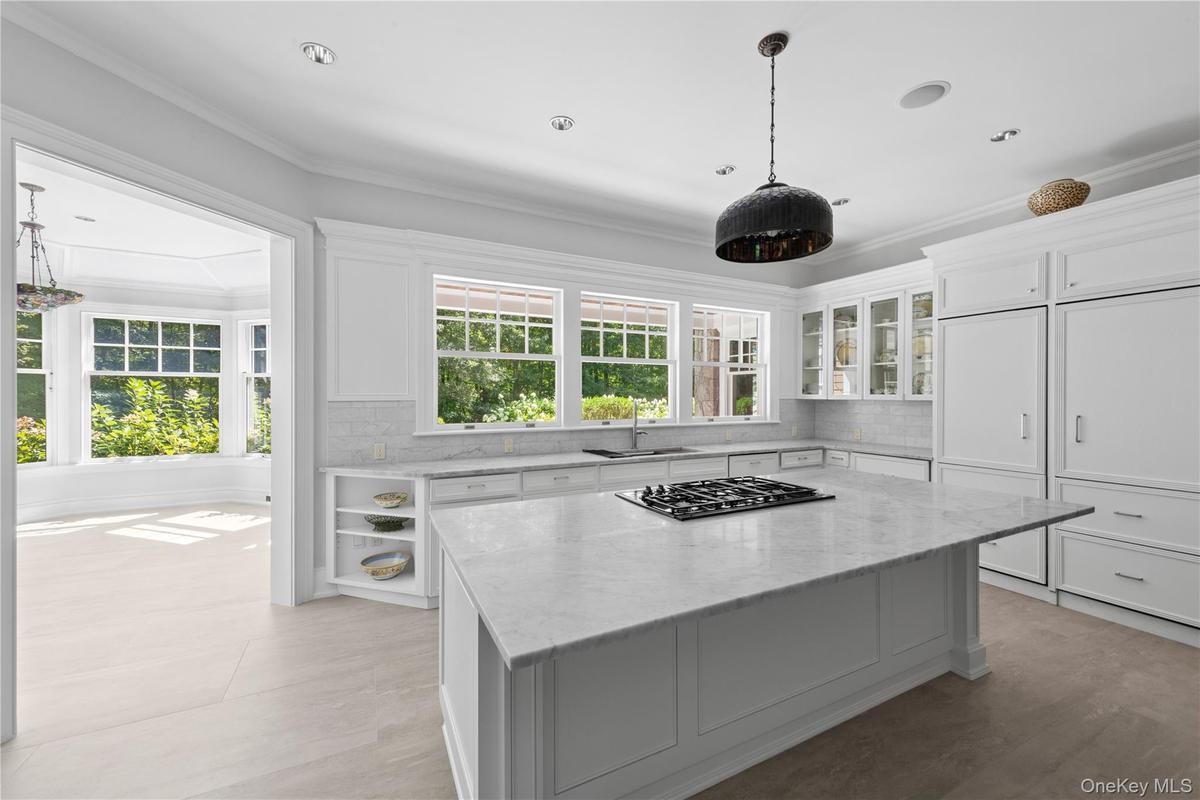 Kitchen featuring decorative backsplash, light stone counters, white cabinets, crown molding, and plenty of natural light