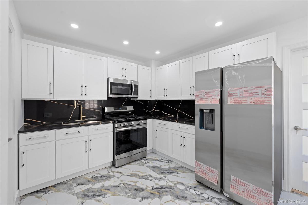 White cabinetry, black countertops with white veining, stainless steel appliances, and recessed lighting