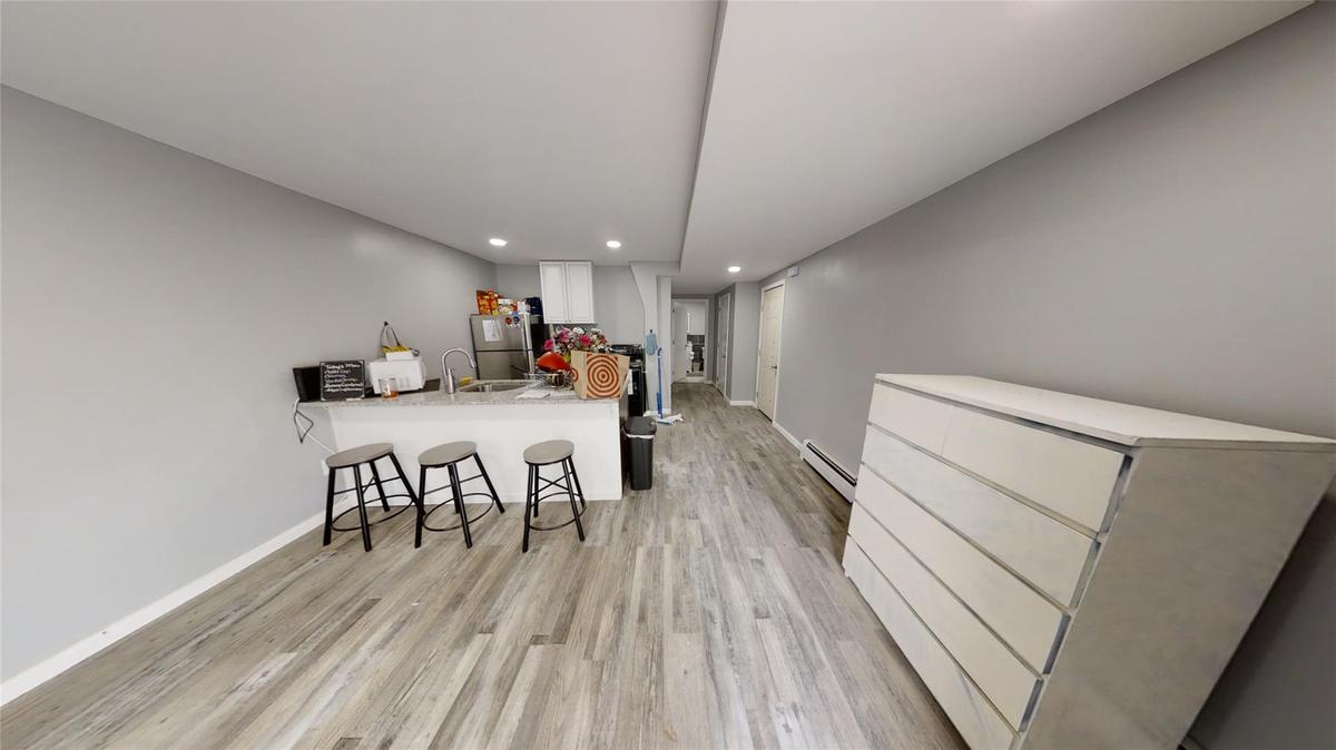 Kitchen featuring a breakfast bar area, stainless steel refrigerator, a baseboard radiator, kitchen peninsula, and white cabinets