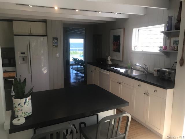 Kitchen with white refrigerator with ice dispenser, a sink, dishwasher, dark countertops, and beamed ceiling