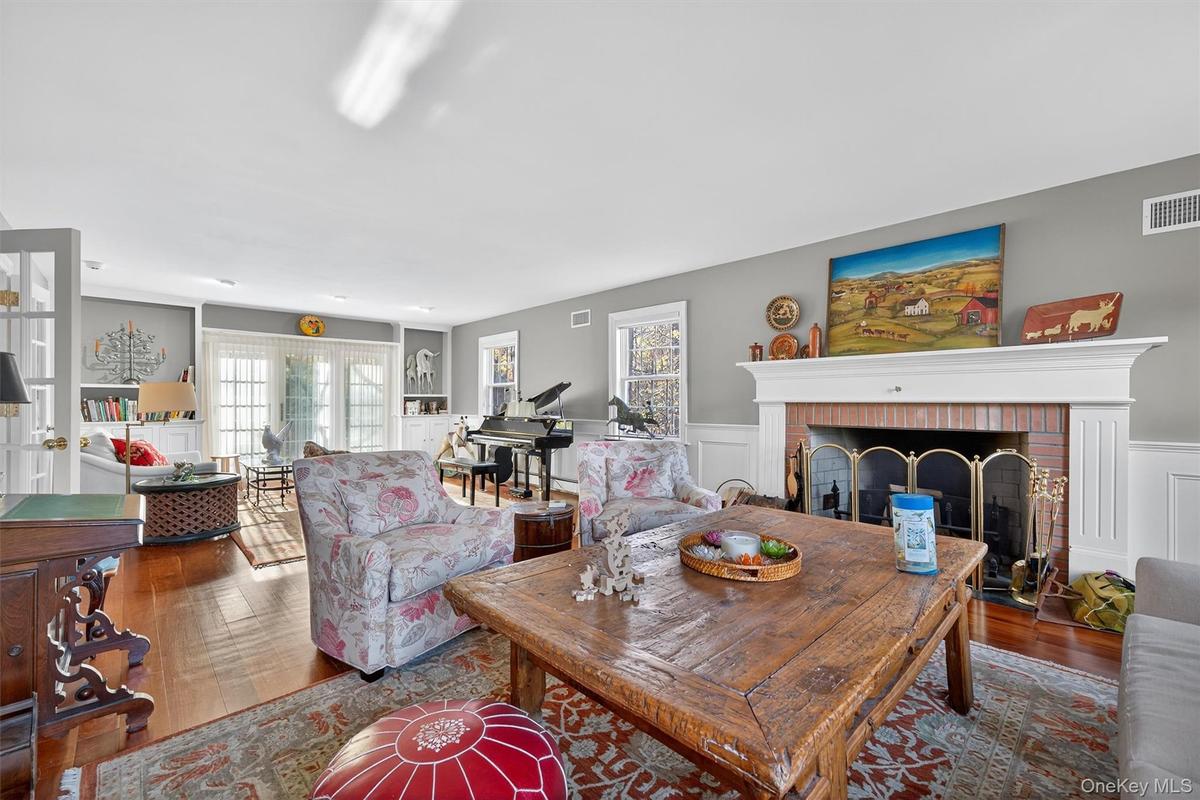 Living room with dark wood-style floors, plenty of natural light, a brick fireplace, a wainscoted wall, and a decorative wall