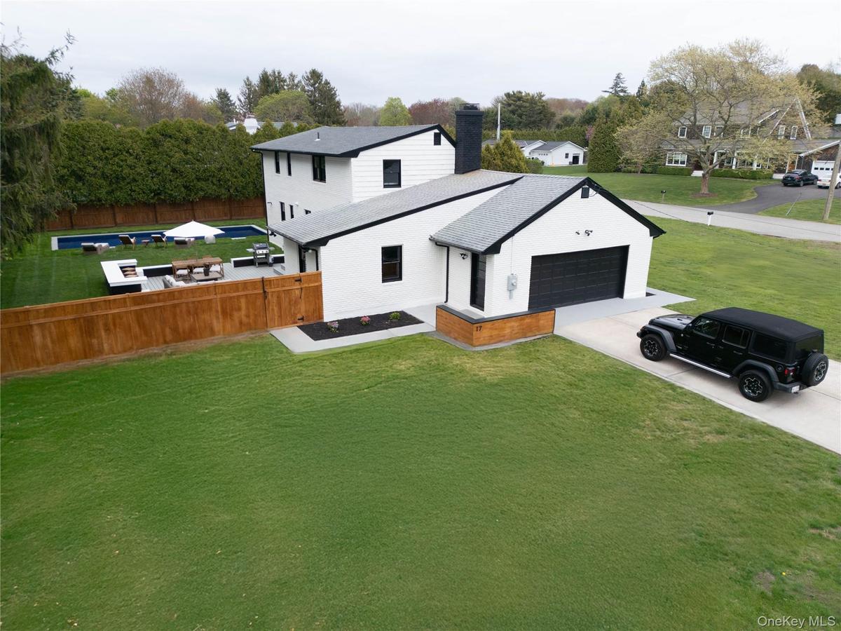 Back of house with concrete driveway, a chimney, an attached garage, brick siding, and view of wooded area