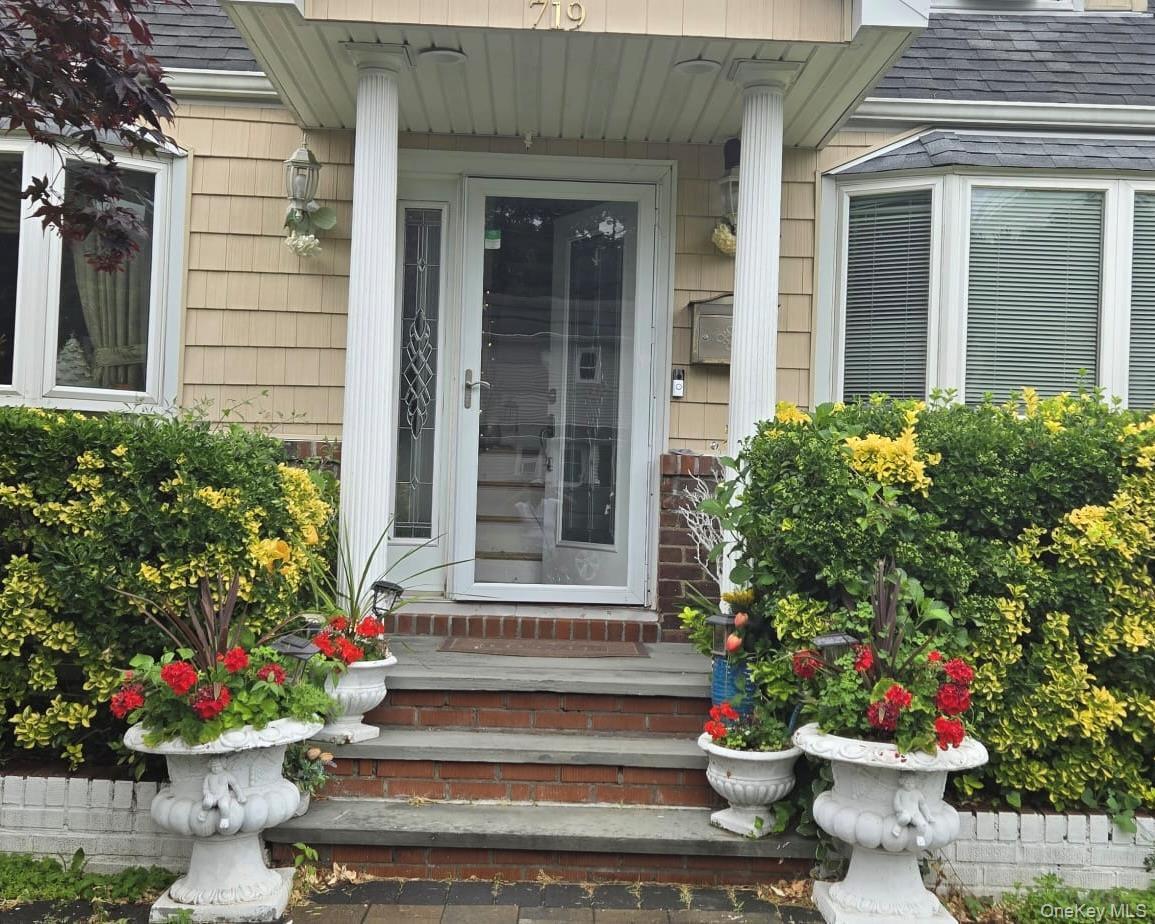 Shingle-sided residence featuring a glass-paneled entry door, two decorative fluted columns, and a multi-pane bay window