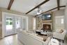 The Living Room is accented by exposed wood ceiling beams, a COZY FIREPLACE, built-in shelving, and NATURAL LIGHT flowing through another set of Frenc