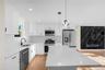 Kitchen featuring a central island with a light-toned countertop, white cabinetry with black hardware, stainless steel appliances, and a white tiled b