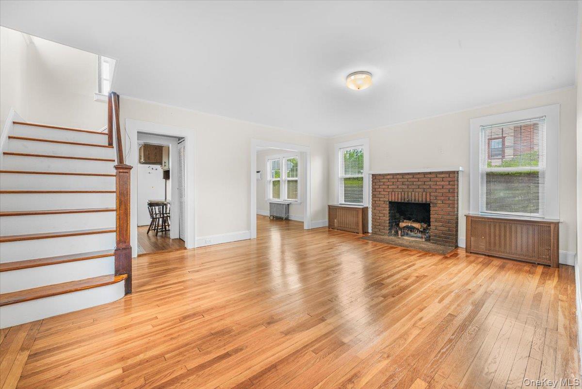 Large living room with wood burning fireplace, 3 windows allowing generous natural light, Hardwood flooring.