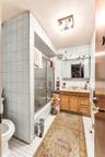 Bathroom featuring white square wall and floor tiling, a single-sink wood vanity with a light-toned countertop, and a shower-tub combination with slid