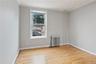 Room featuring wood flooring, neutral wall paint, a double-hung window, and a radiator heating unit