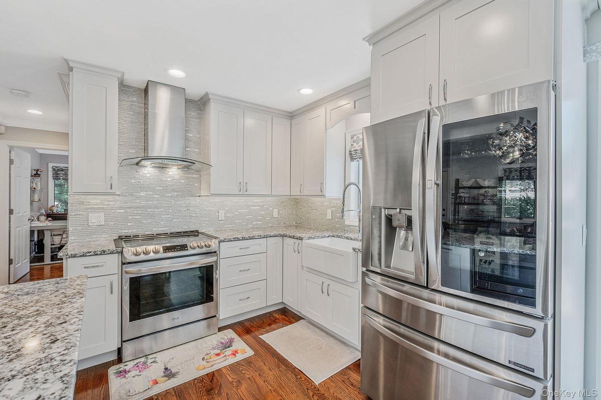 Kitchen with stainless steel appliances, wall chimney range hood, white cabinetry, dark wood-style floors, and light stone counters