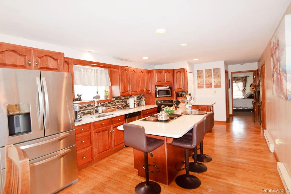 Open-concept kitchen featuring wood-finish cabinetry, stainless steel appliances, a center island with countertop seating, and wood-finish flooring