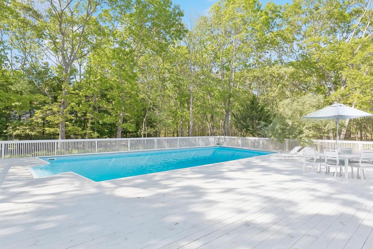 View of pool featuring view of scattered trees, a patio, and a deck