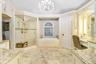 Amazing master bathroom with beautiful custom lighting and chandelier with steam shower, vanity area, large Roman soaking tub, and his and her sink ar
