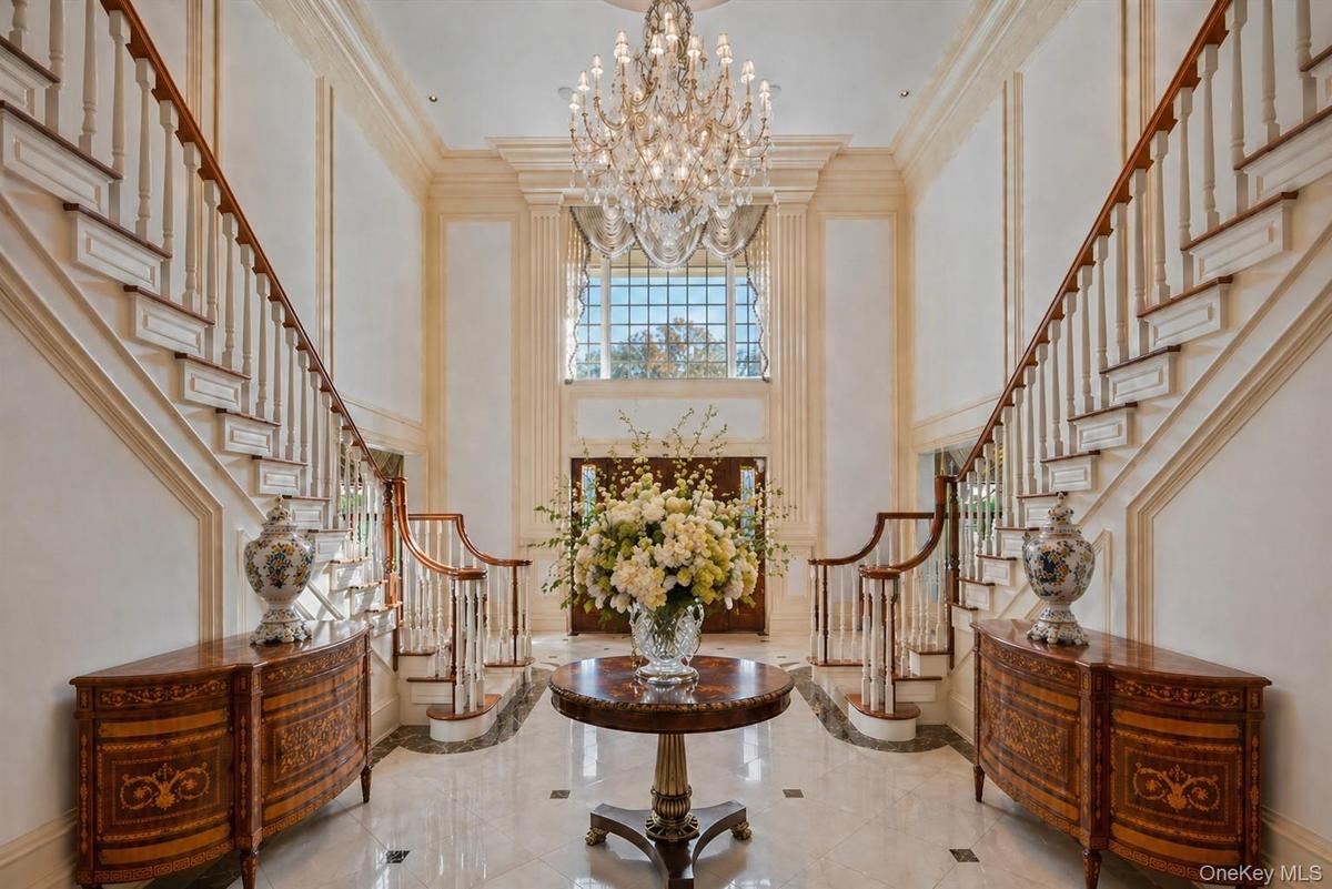Grand foyer featuring a dual staircase with wood handrails, a large multi-tiered chandelier, and polished tile flooring with contrasting accents
