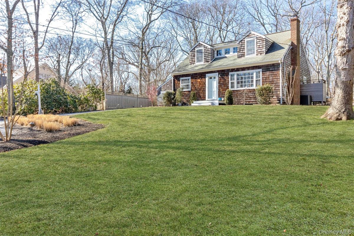 View of front of house featuring roof with shingles, a chimney, a front yard, and fence