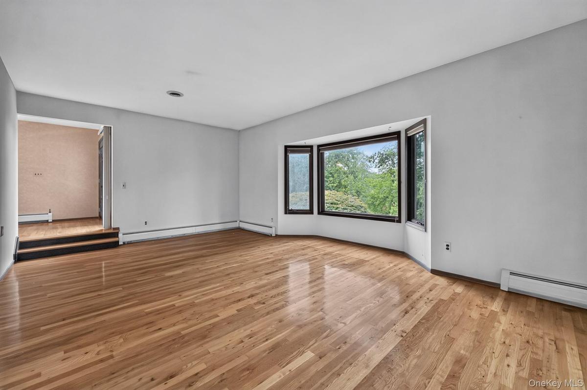 An expansive, formal step-down living room with soaring high ceilings, freshly polished solid hardwood floors, and a large architectural bow window le
