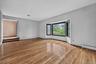 An expansive, formal step-down living room with soaring high ceilings, freshly polished solid hardwood floors, and a large architectural bow window le
