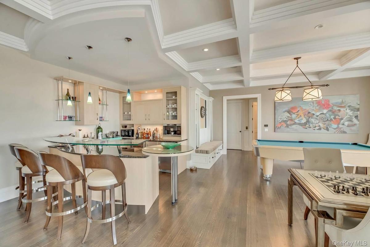 Indoor wet bar with decorative light fixtures, beam ceiling, coffered ceiling, glass insert cabinets, and dark wood-type flooring