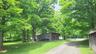 Gravel driveway surrounded by mature trees, leading to a wood-sided outbuilding