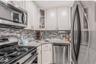 Kitchen with appliances with stainless steel finishes, glass insert cabinets, light stone countertops, white cabinets, and decorative backsplash