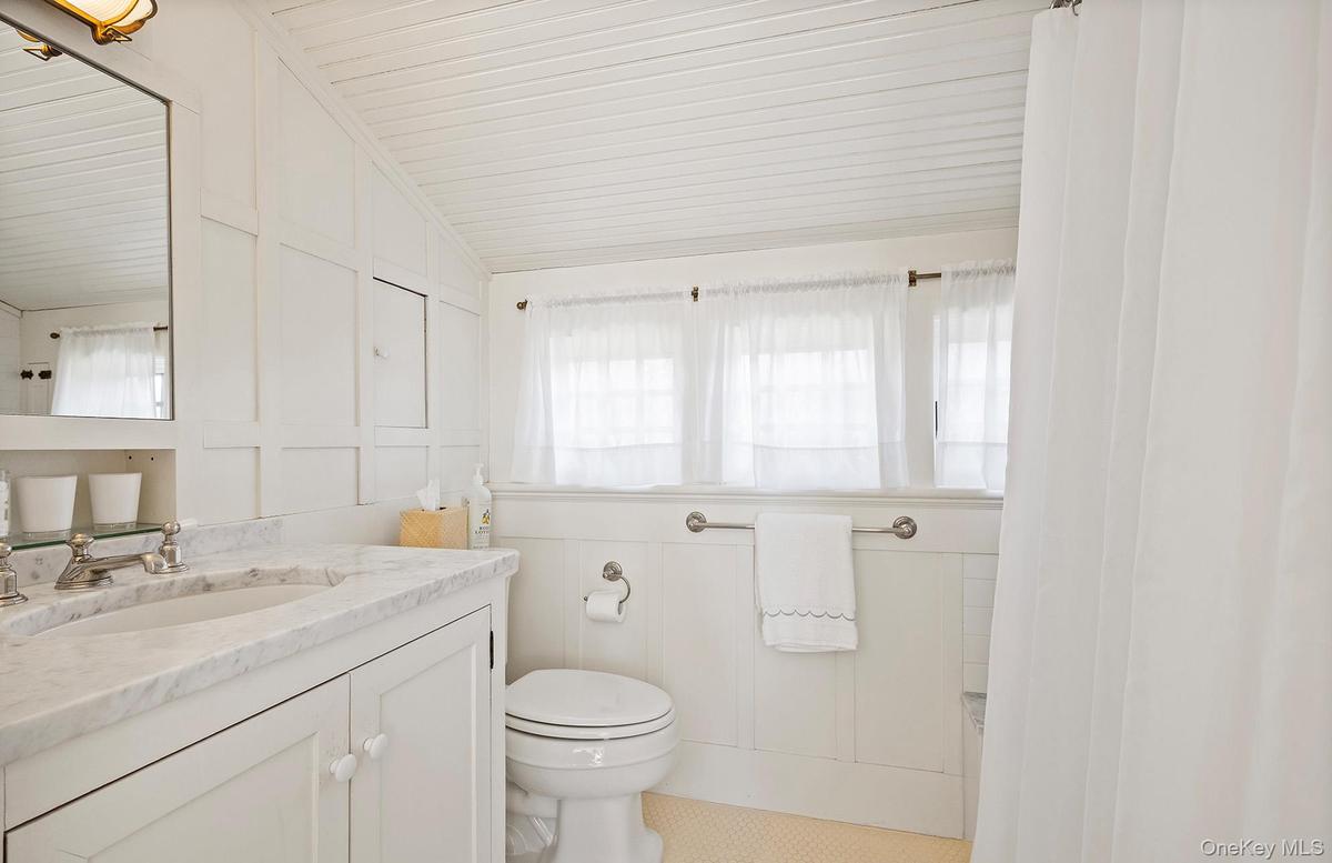 Bathroom featuring a decorative wall, vanity, toilet, and lofted ceiling