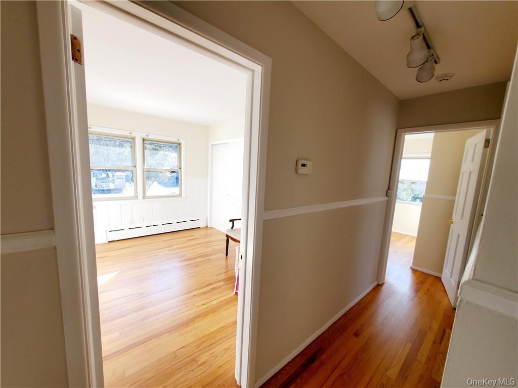 Corridor with a baseboard heating unit, track lighting, and light wood-type flooring