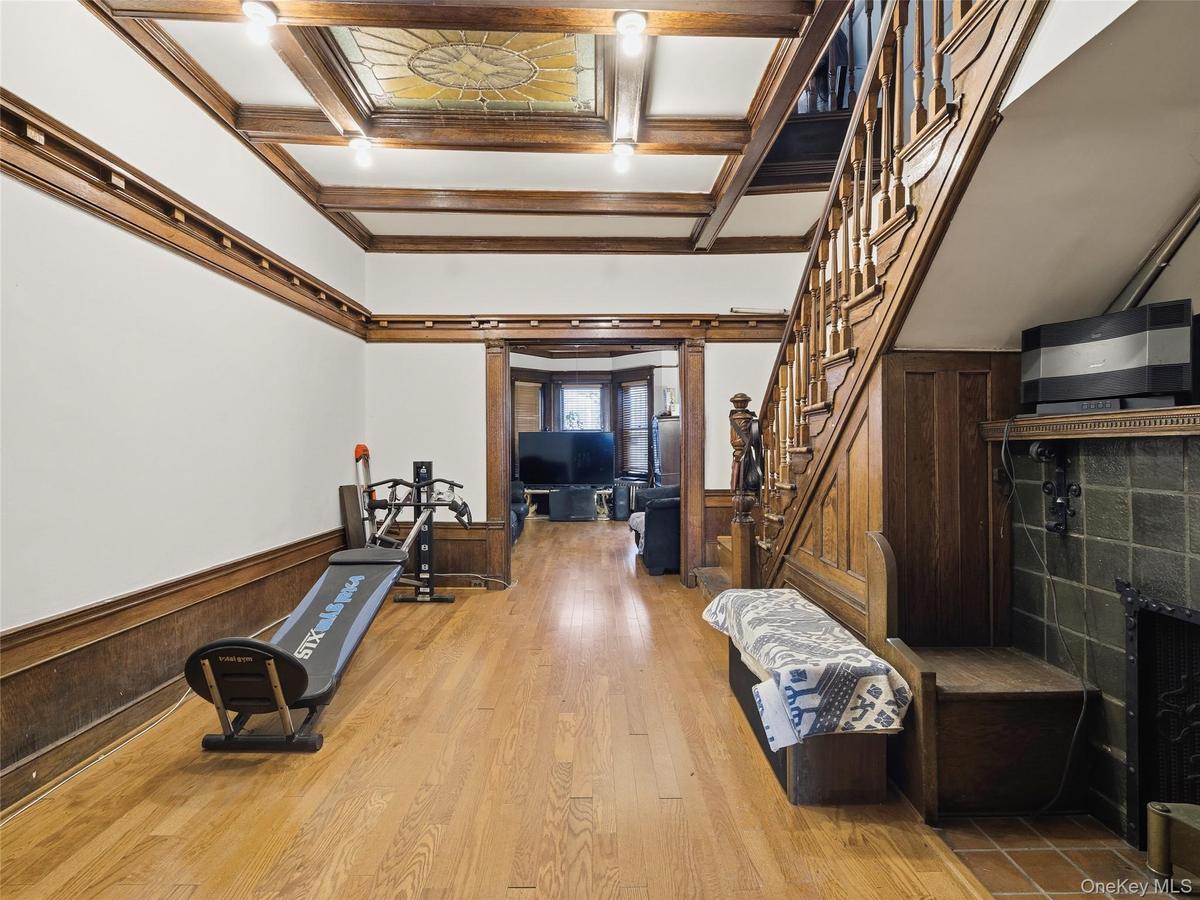 Exercise room featuring a wainscoted wall, wood walls, coffered ceiling, light wood-type flooring, and a fireplace