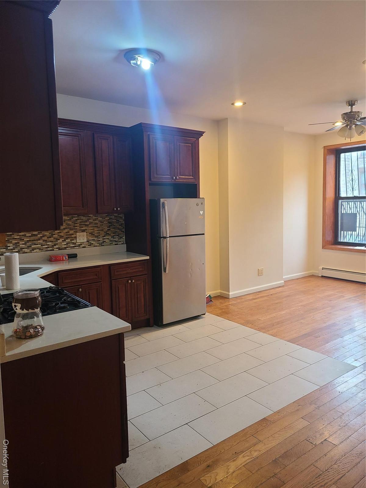 Kitchen with light countertops, cooktop, freestanding refrigerator, tasteful backsplash, and ceiling fan