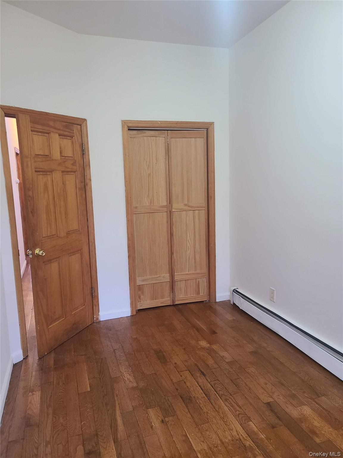Unfurnished bedroom with baseboards, dark wood-style flooring, and a baseboard heating unit