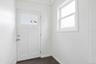 Entryway featuring a white paneled door with integrated glass panes, a single-hung window with white trim, dark wood-finish flooring, and light-toned 