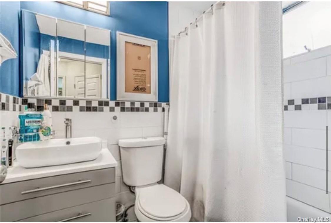 Full bath featuring vanity, tile walls, and shower / tub combo with curtain