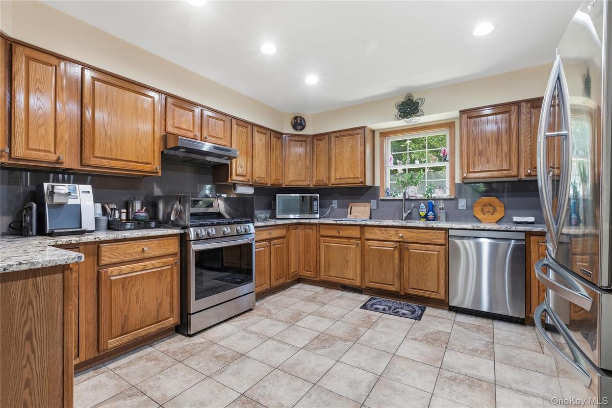 Kitchen featuring wood cabinetry, stainless steel appliances, granite-style countertops, and a tile floor