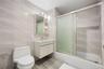 Full bathroom with tile walls, shower / bath combination with glass door, toilet, and vanity