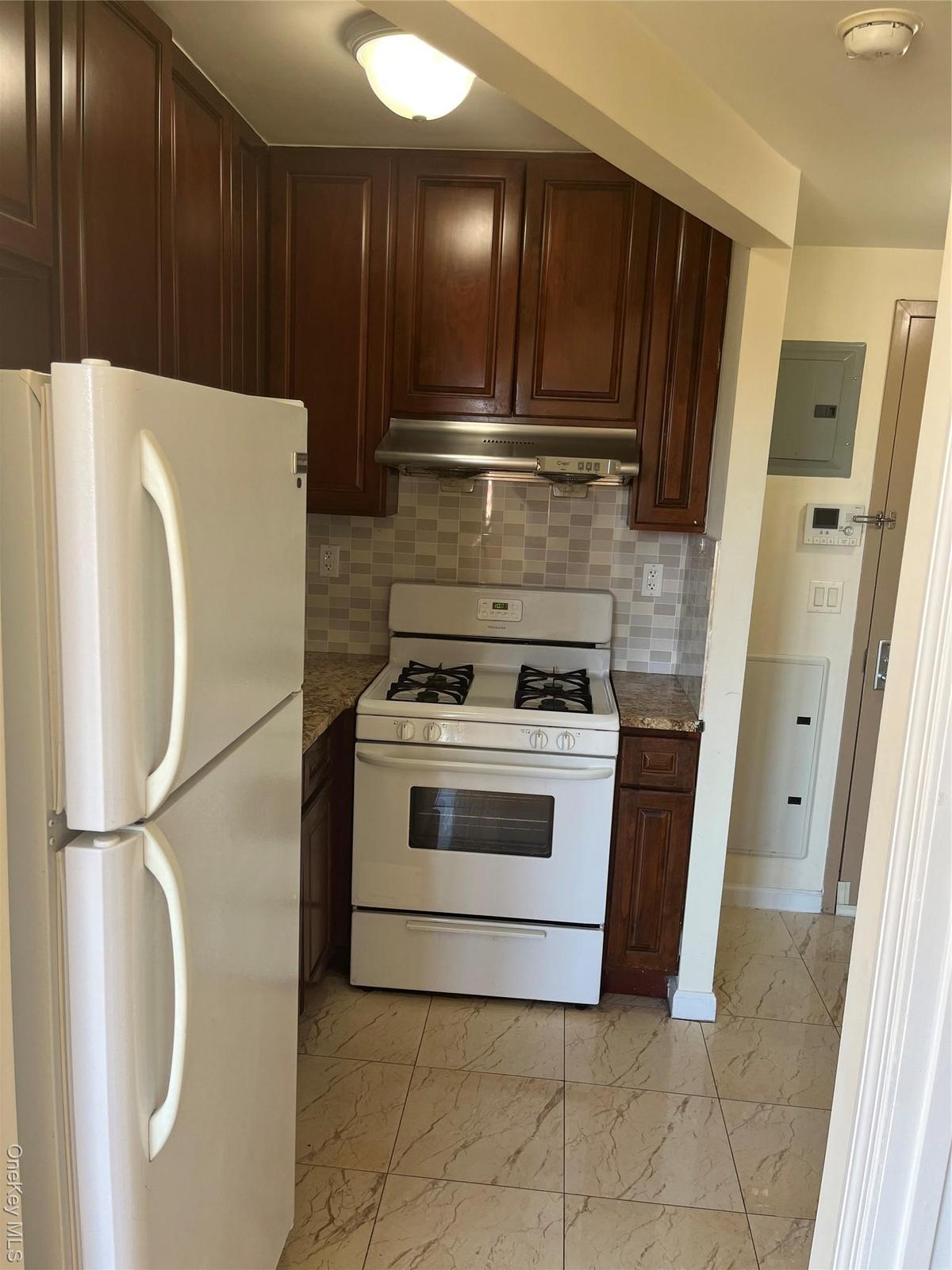 Kitchen with refrigerator, gas range gas stove, backsplash, dark brown cabinetry, and light marble finish flooring
