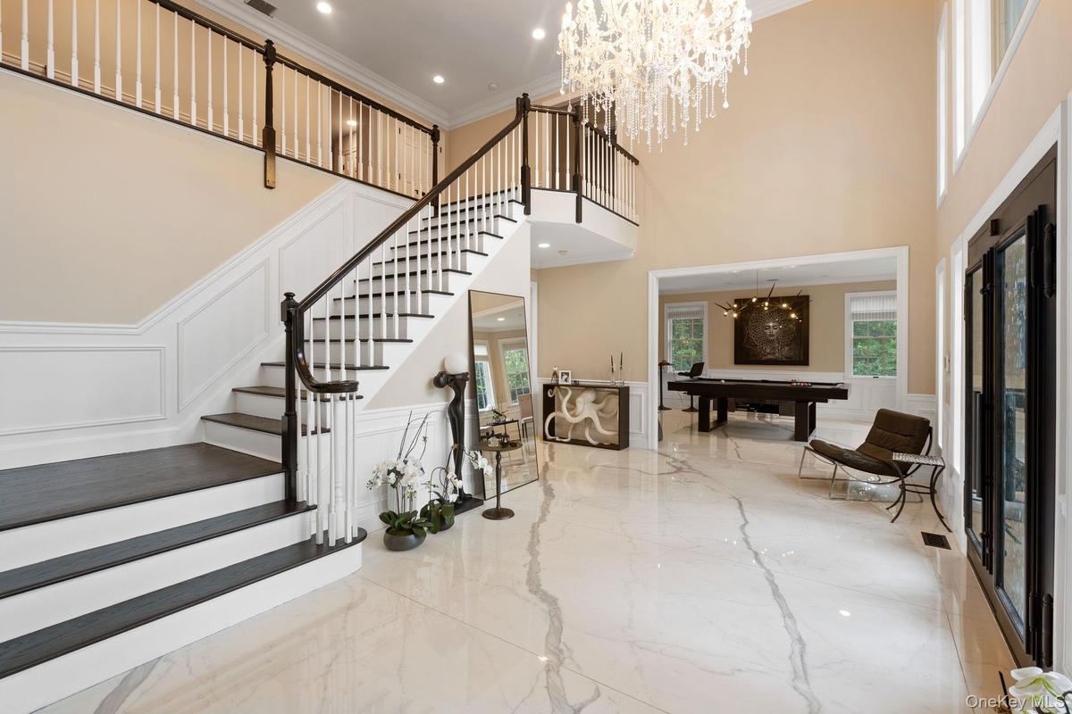 Entryway featuring a decorative wall, marble tiled floors, a chandelier, ornamental molding, and a wainscoted wall