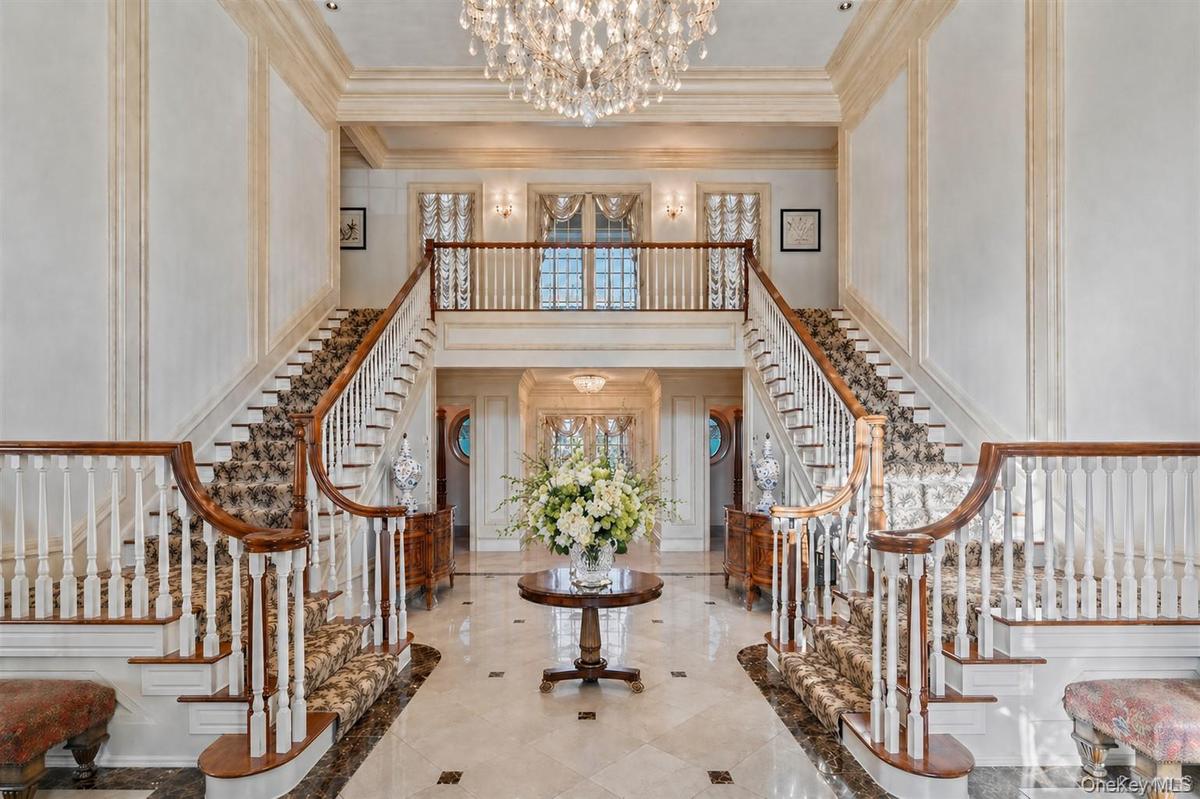Grand foyer featuring a dual curved staircase with patterned carpet runners, hardwood handrails, and white balusters