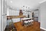Kitchen featuring extensive white cabinetry, a central island with countertop, a stainless steel refrigerator, wood-finish flooring, and pendant light