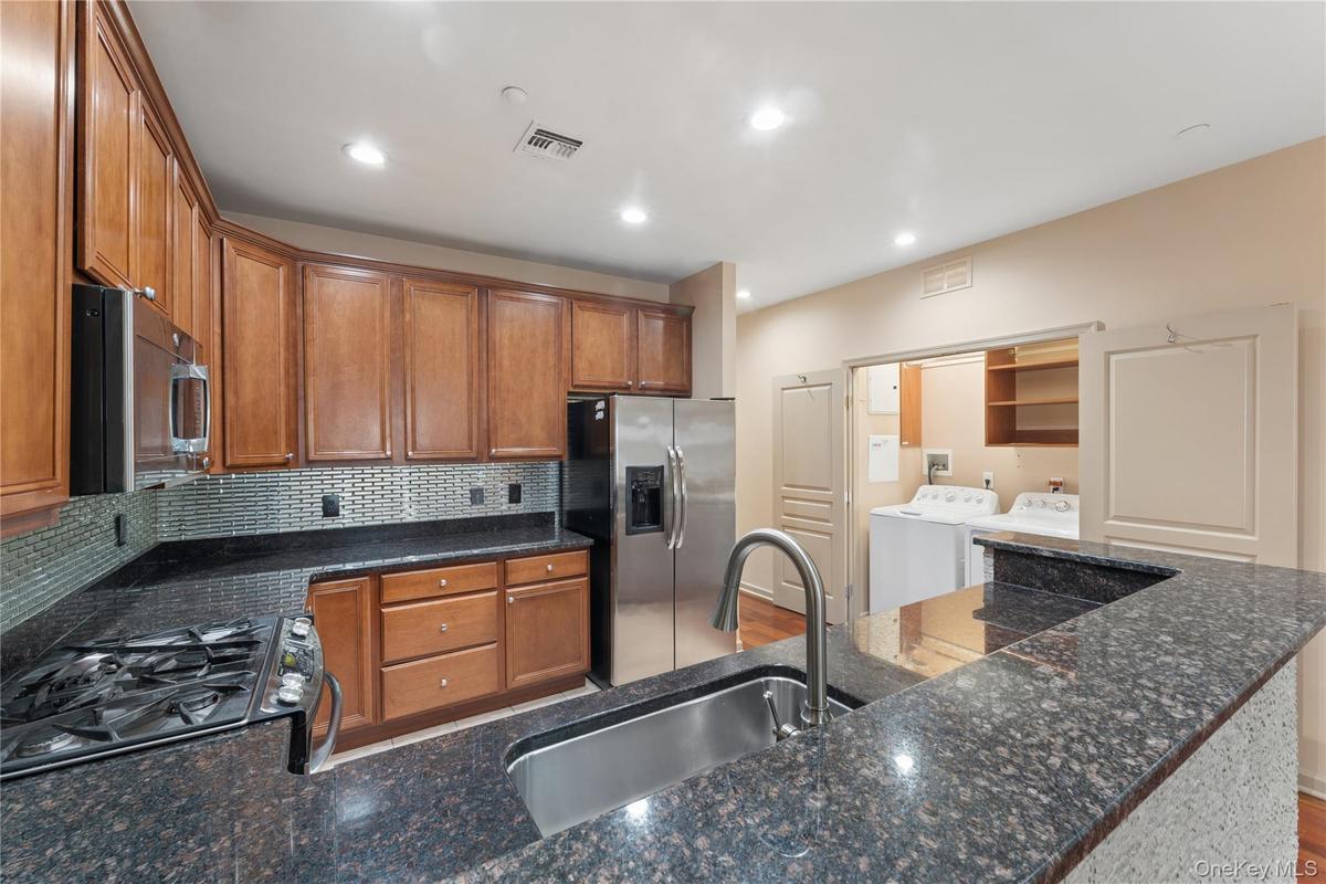 Kitchen featuring rich wood cabinetry, stainless steel appliances, dark granite-finish countertops, and a tile backsplash