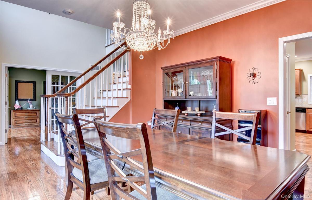 Hardwood flooring throughout the dining area, featuring a tiered crystal chandelier, crown molding, and a staircase with white risers and wood handrai
