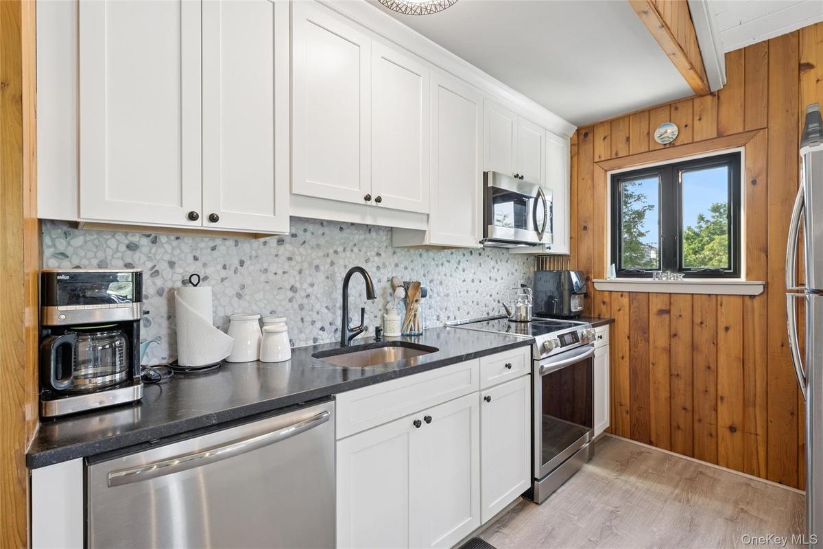 Modern kitchen featuring white shaker cabinetry, stainless steel appliances, dark countertops, a pebble-style backsplash, and wood-finish flooring