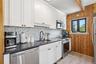 Modern kitchen featuring white shaker cabinetry, stainless steel appliances, dark countertops, a pebble-style backsplash, and wood-finish flooring