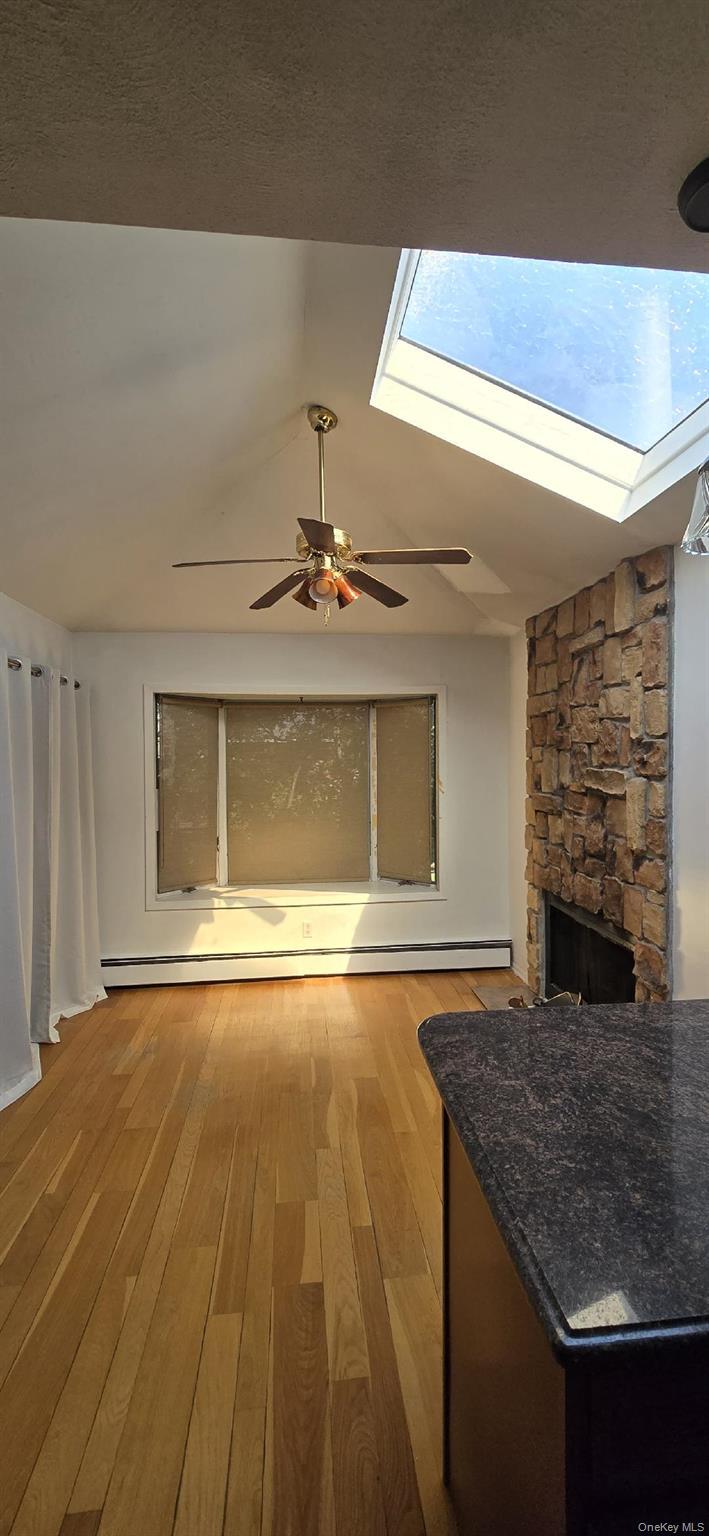 Living area featuring a vaulted ceiling with a skylight, a ceiling fan, and wood-finish flooring