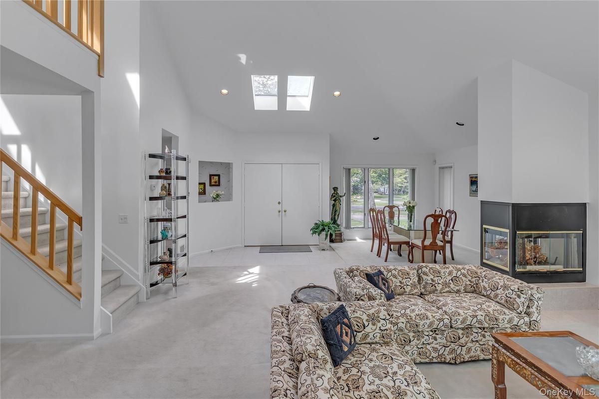 Vaulted ceiling interior featuring skylights, a carpeted staircase with wood handrails, a multi-sided fireplace with a black surround, and a dining ar
