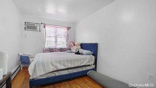 Bedroom with wood finished floors, a baseboard heating unit, and an AC wall unit