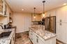Kitchen featuring a central island with a stone-finish countertop, stainless steel appliances, extensive cabinetry with contrasting hardware, recessed