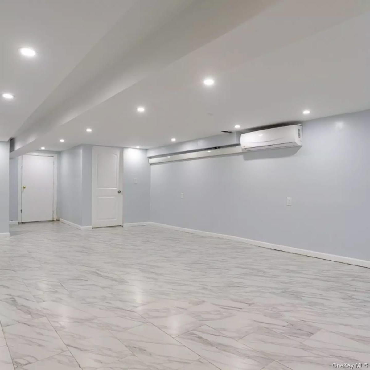 Finished basement with light marble finish floors, recessed lighting, and a wall mounted AC