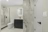 Contemporary bathroom featuring a dark vanity with a white countertop, a lighted mirror, and a frameless glass shower enclosure