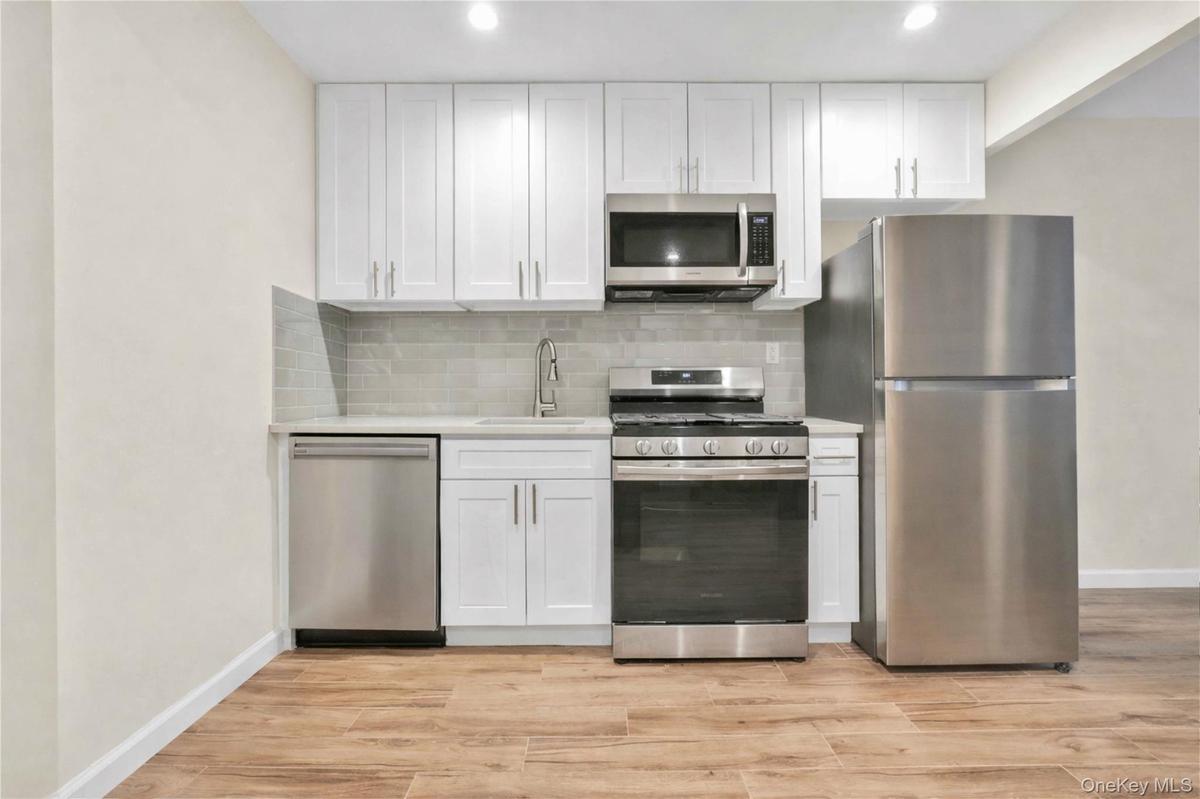 Kitchen featuring stainless steel appliances, white cabinetry, light wood-type flooring, decorative backsplash, and light stone counters